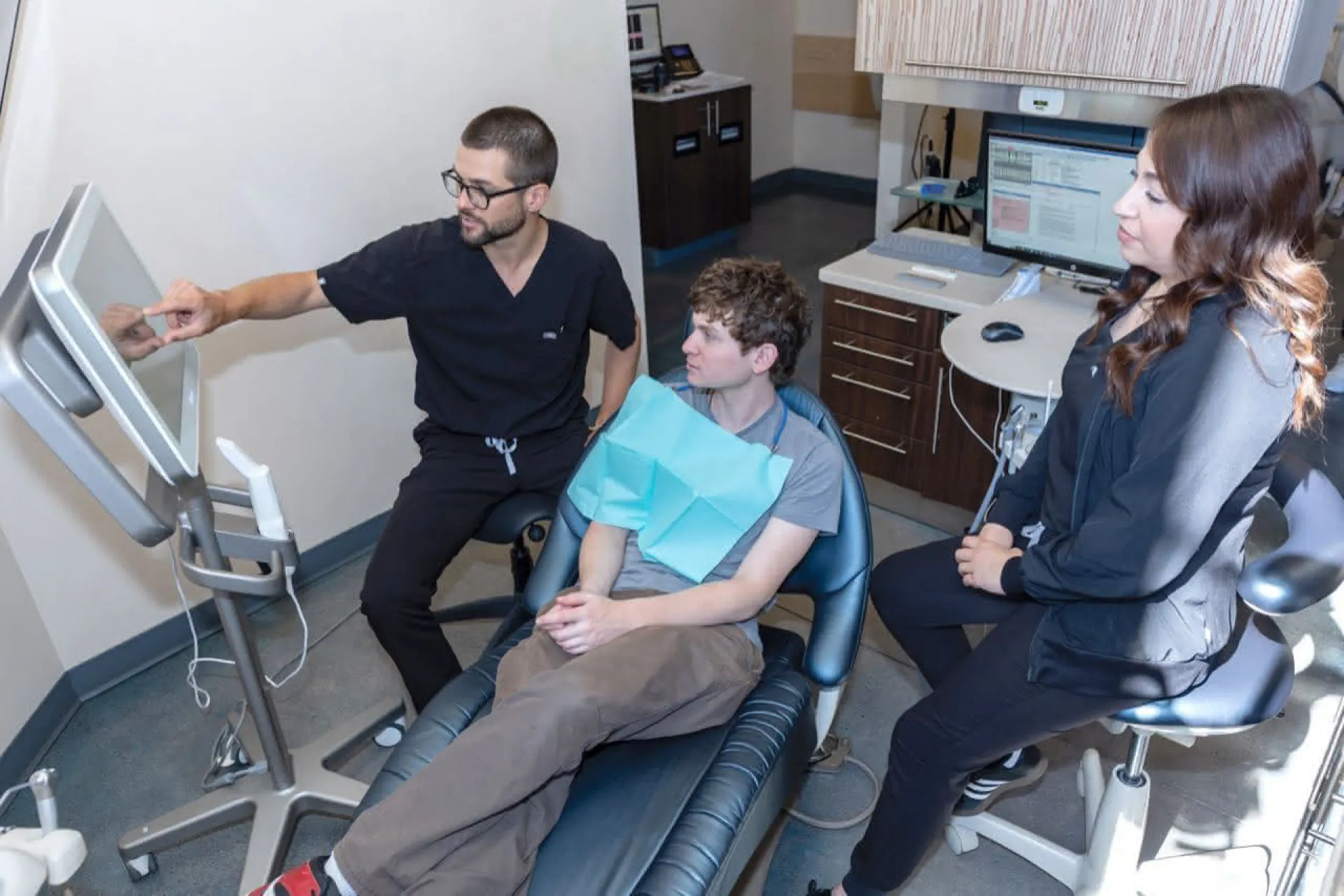 A doctor pointing at a monitor with a patient in a chair