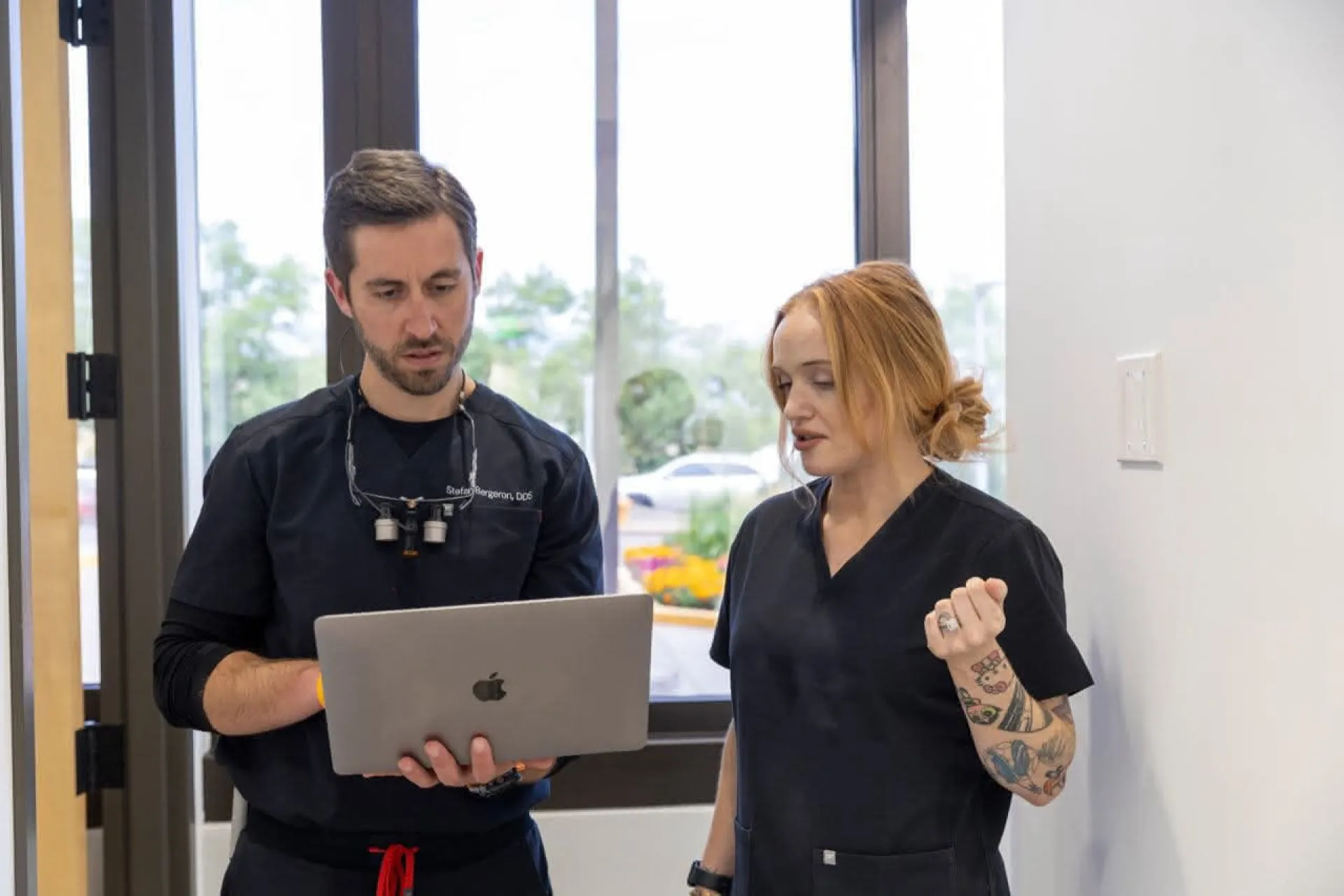 A dentist holding a laptop with a dental assistant in the hallway