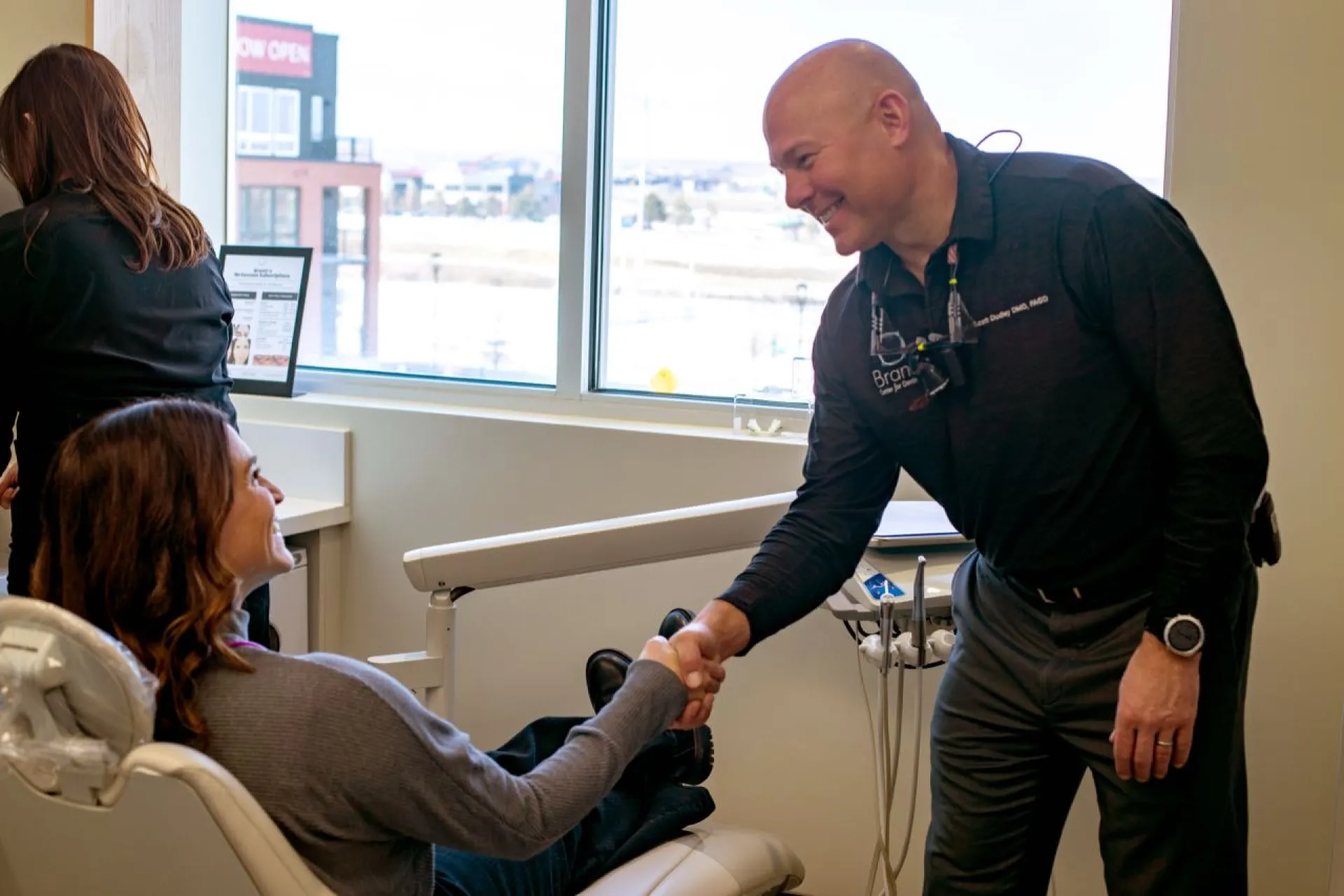 A patient in an exam chair shaking hands with Dr. Dudley