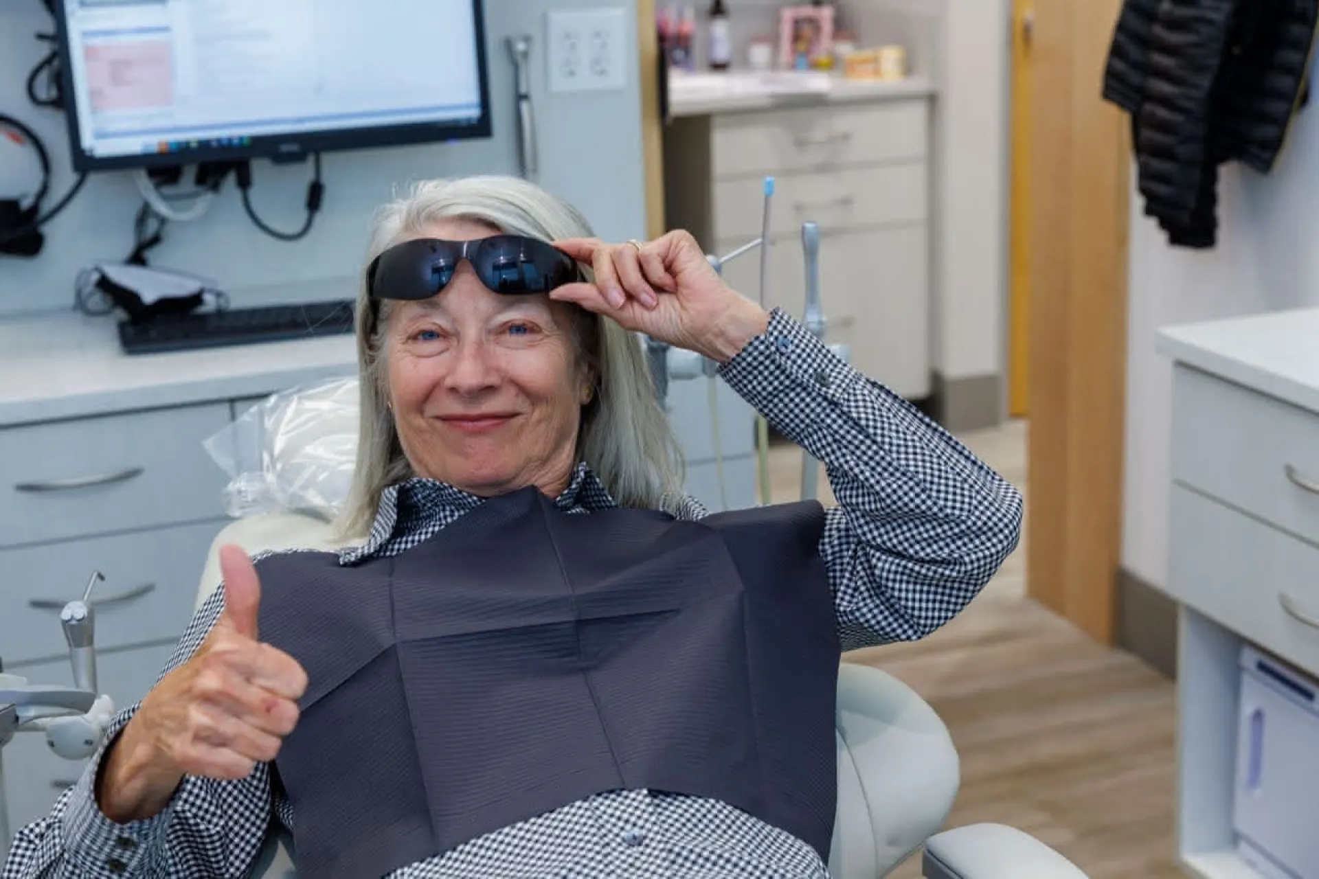 A patient lifting a pair of sunglasses giving a thumbs up