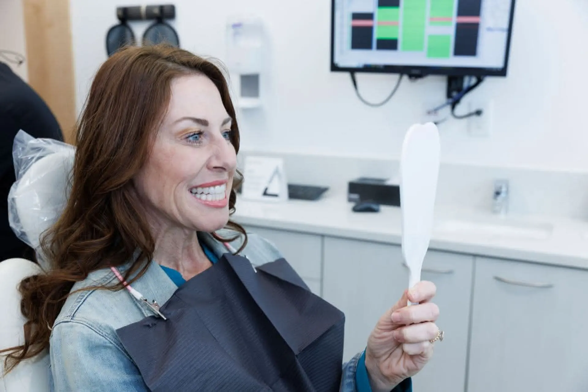 A patient holding a hand mirror smiling